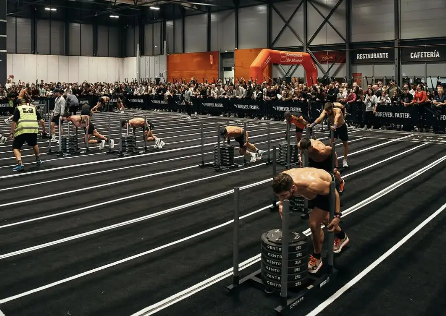 Competición Hyrox con atletas en acción en zona de carrera y workouts.